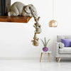 A resin figurine of an elephant hugging a baby, hanging from a wooden shelf.