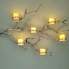 A decorative light fixture featuring branches with glowing LED tea light candles.