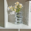 A clear glass vase filled with white daisies and surrounded by stacked mirror tile disco balls.