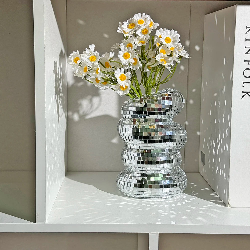 A clear glass vase filled with white daisies and surrounded by stacked mirror tile disco balls.