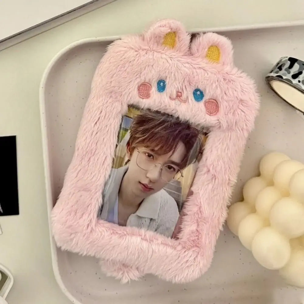 A pink fluffy plush photocard holder shaped like a cat face with blue eyes and pink ears.