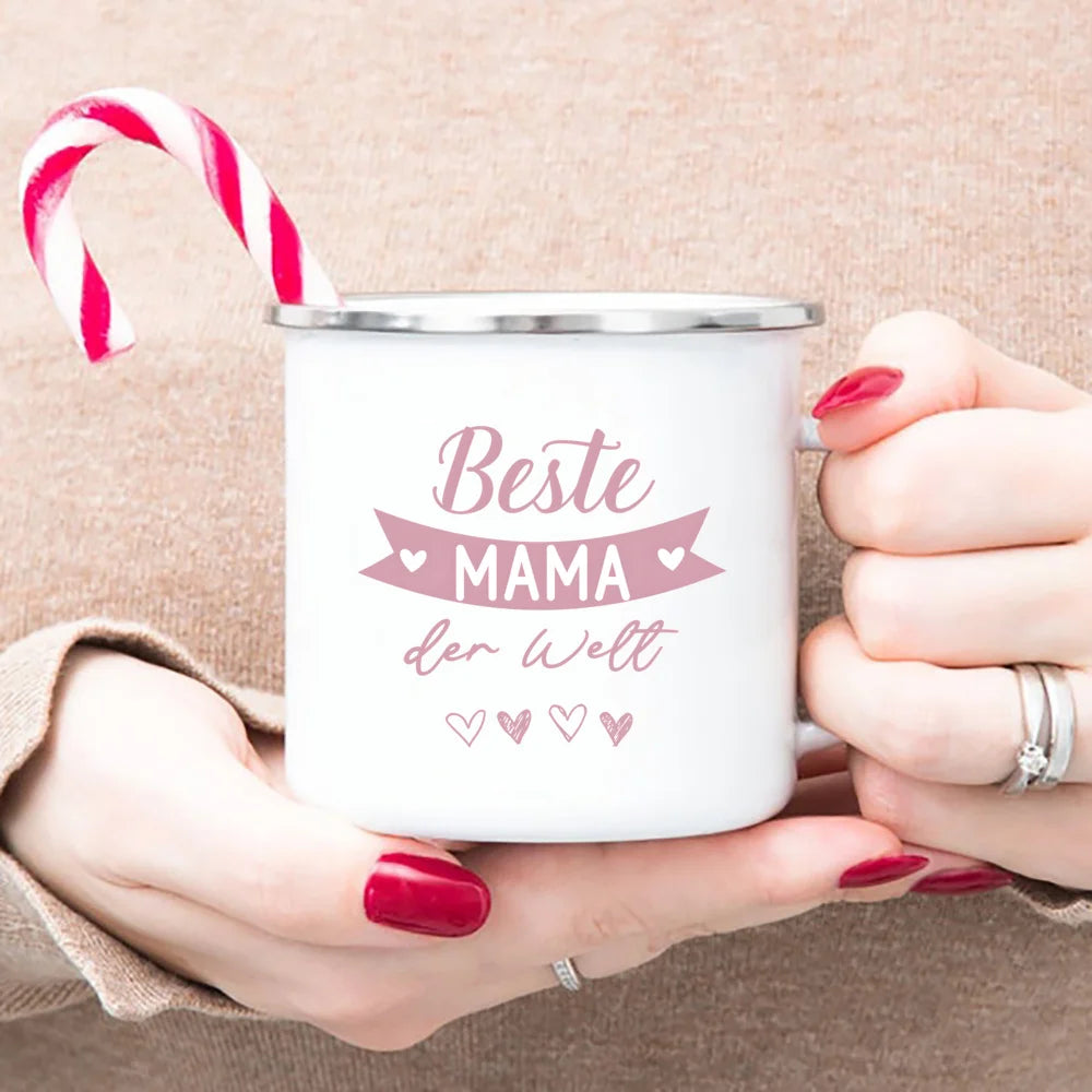 A white enamel mug with pink text reading Beste Mama der Welt is held by a person against a beige background.