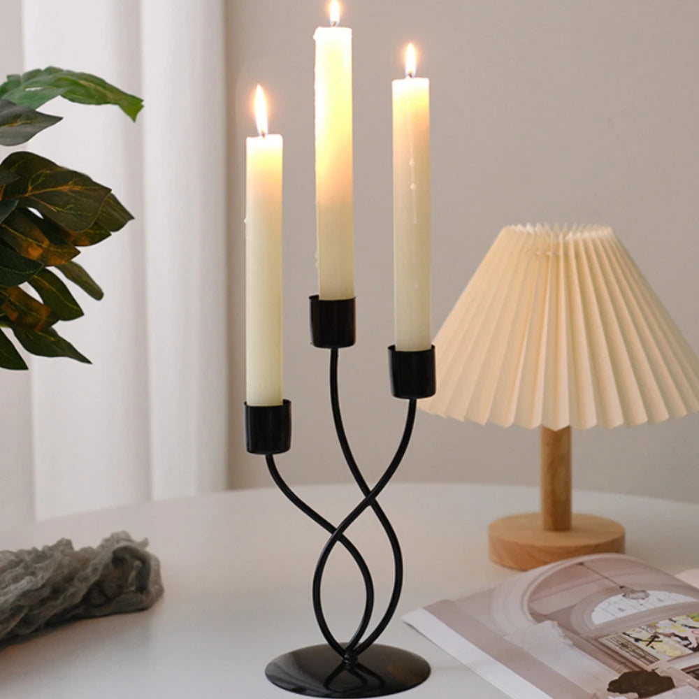 A black iron candle holder with three white taper candles on a white table.