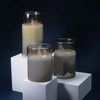 A set of three pillar candles in varying shades of beige and gray displayed on white blocks.