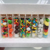 A row of mini glass bottles with cork stoppers filled with colorful candies and various colored candies.