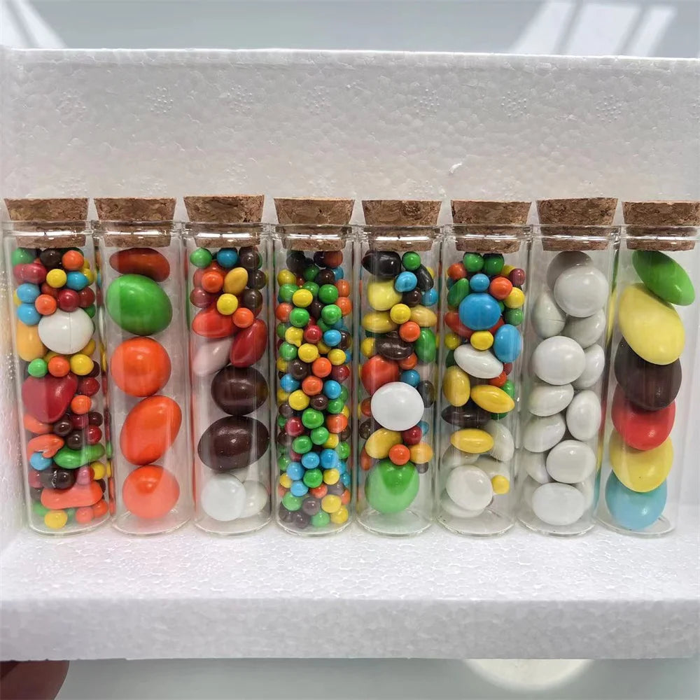 A row of mini glass bottles with cork stoppers filled with colorful candies and various colored candies.