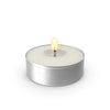 A silver tin candle holder with a lit yellow flame and white wax inside.