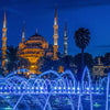 Night view of a mosque with minarets and a fountain display.