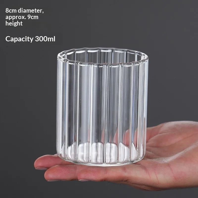 A clear cylindrical glass vase with vertical ridges is held in a hand.