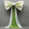 A white satin bow with green foliage and a long sheer tulle drape for event decoration.
