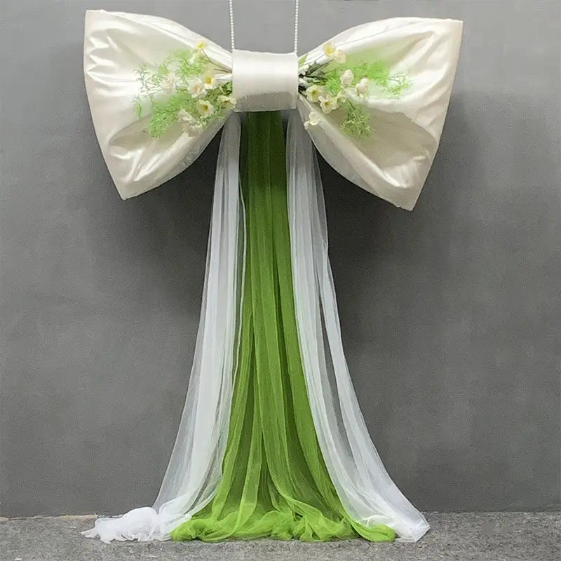 A white satin bow with green foliage and a long sheer tulle drape for event decoration.