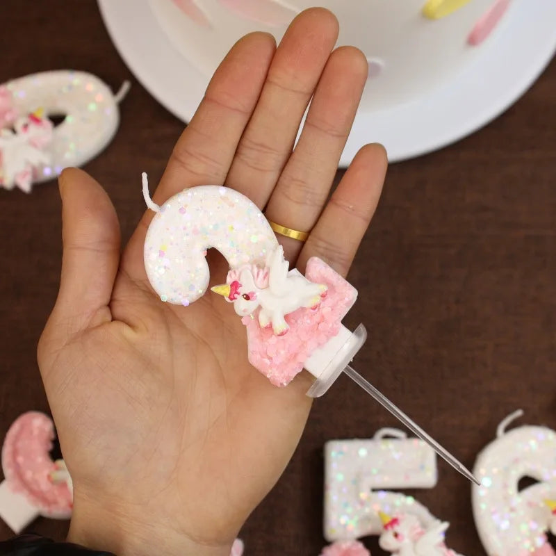 Una mano sostiene una vela con forma de nueve, blanca y brillante, decorada con toques rosas.