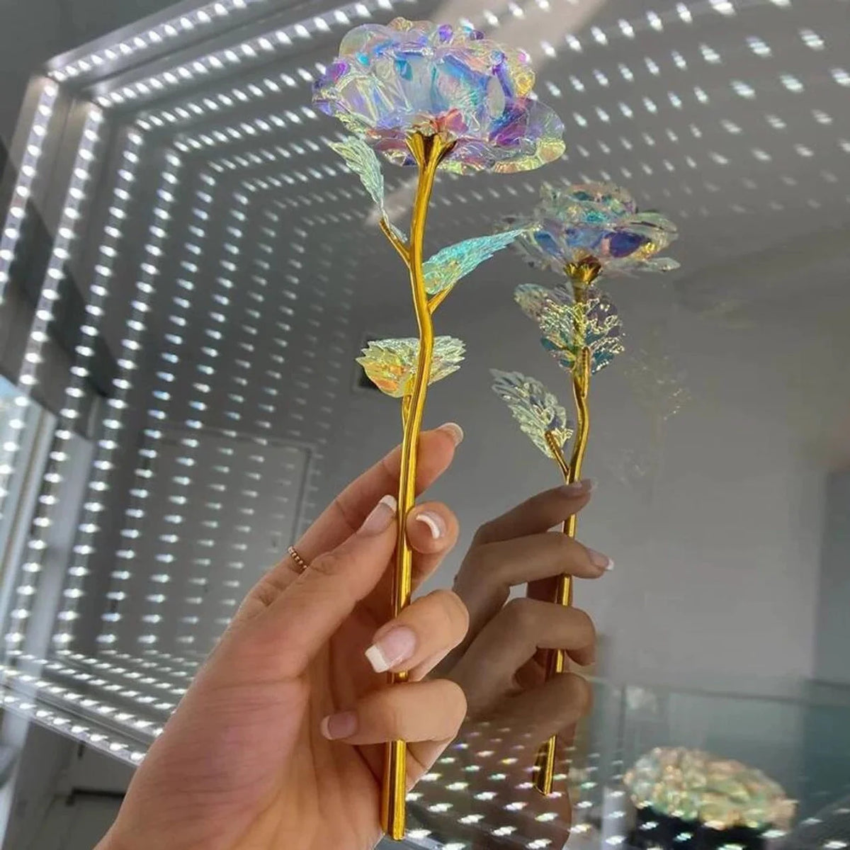 A hand holds a tall, golden stem with purple and green artificial crystal flowers against a bright background.