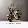 A black and white ceramic vase with a geometric circle pattern sits on a white surface.