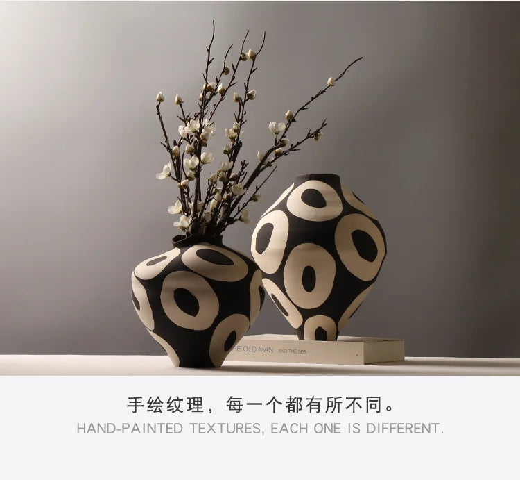 A black and white ceramic vase with a geometric circle pattern sits on a white surface.