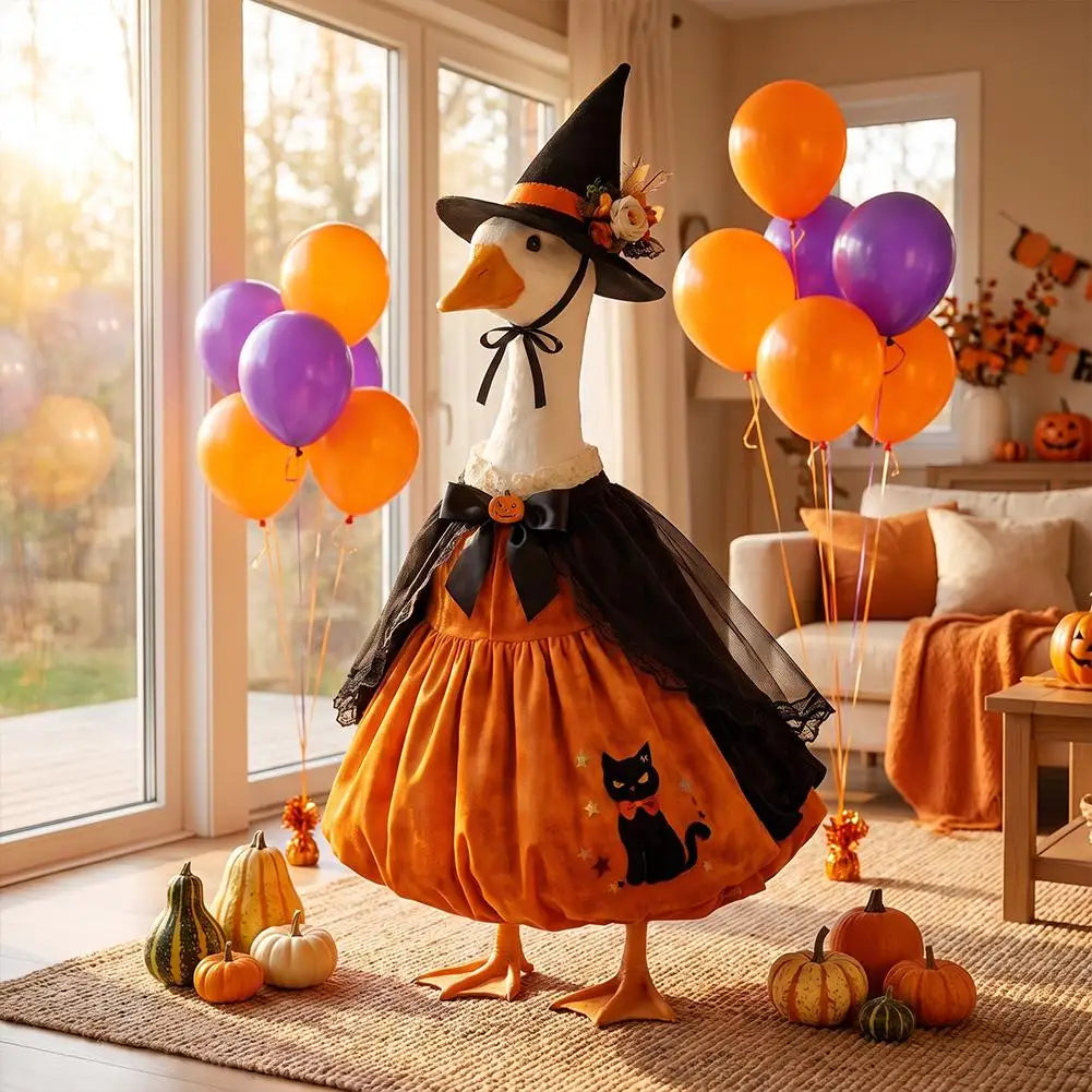 A decorative Halloween lawn goose costume featuring an orange body, black cape, and witch hat, displayed indoors near a windo