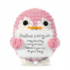 A pink crocheted penguin doll holding a white card with the message I may be a tiny penguin but I believe in you Go do your t