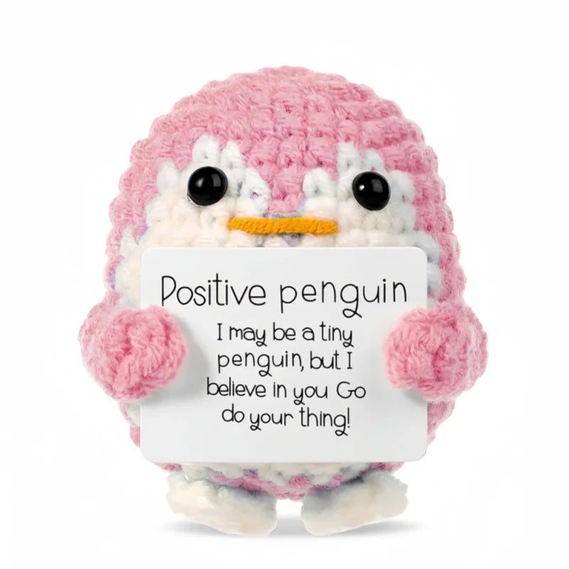 A pink crocheted penguin doll holding a white card with the message I may be a tiny penguin but I believe in you Go do your t