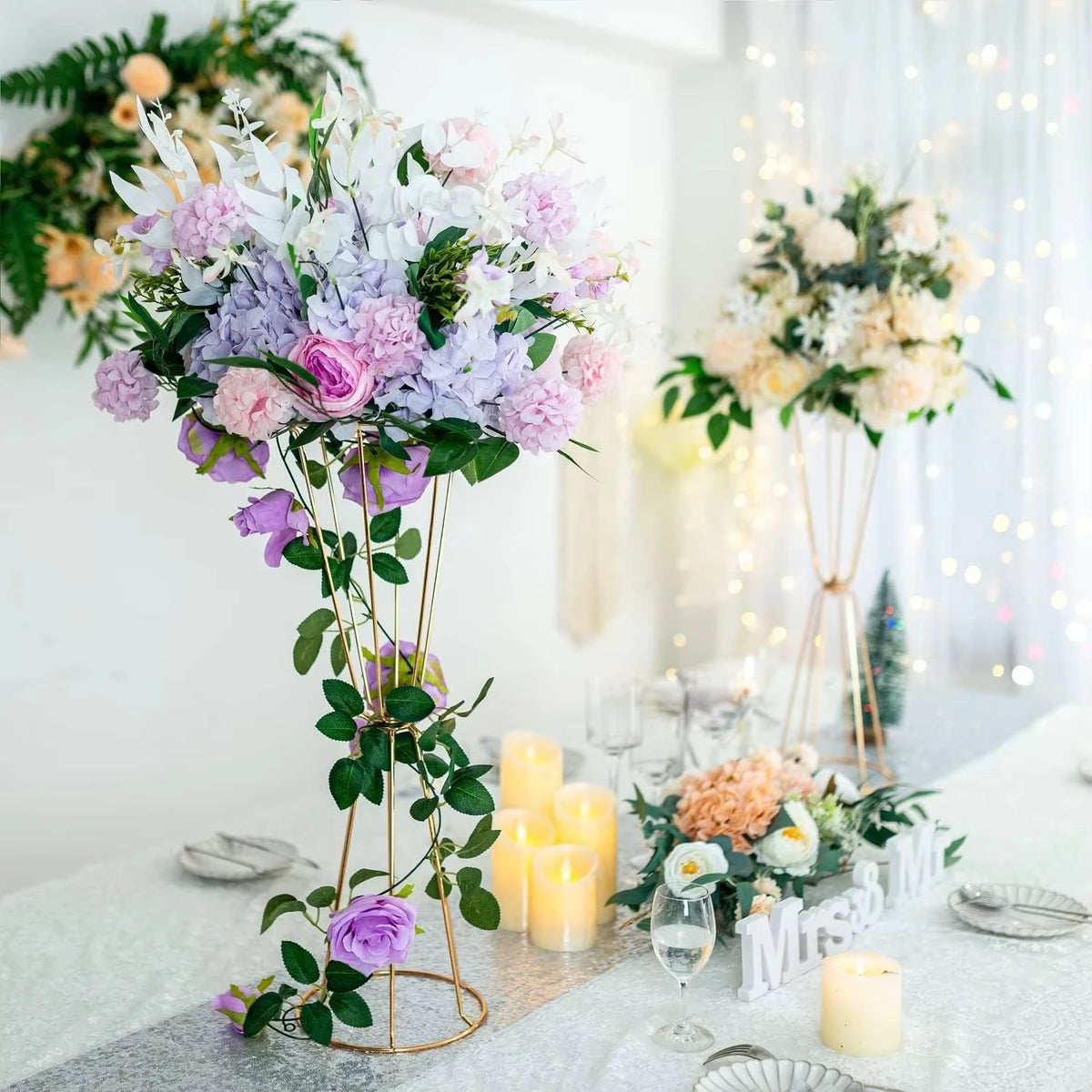 Gold geometric flower stands with white and purple flowers decorating a table.