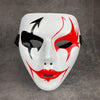 A white masquerade mask with red markings and a black arrow design against a gray background.