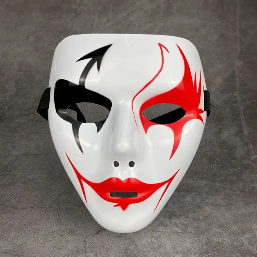 A white masquerade mask with red markings and a black arrow design against a gray background.