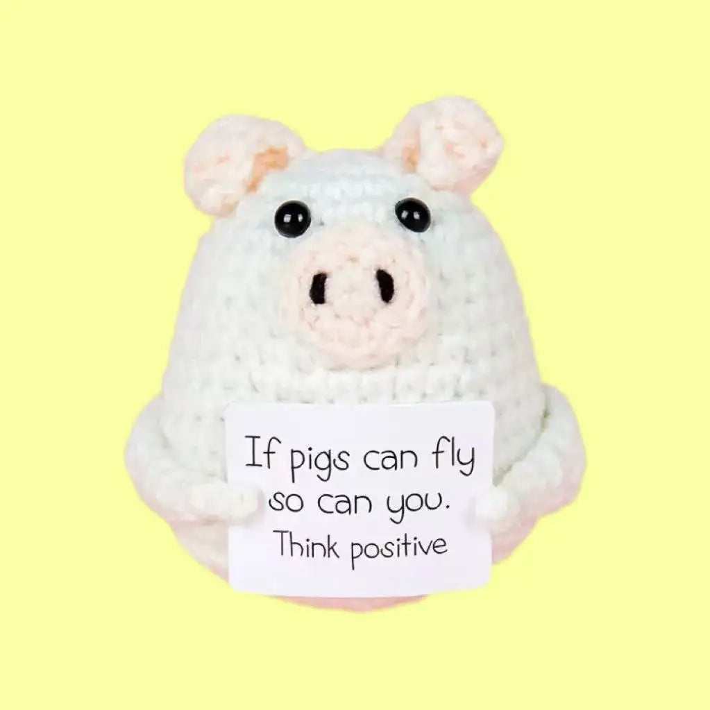 A handmade crochet pig doll with a positivity card on a light yellow background.