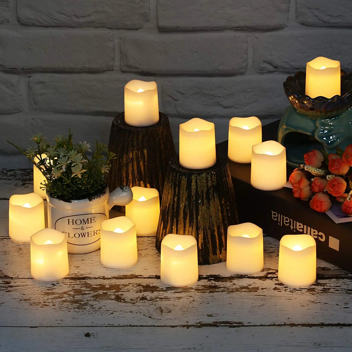 A collection of glowing white LED tea light candles arranged on a rustic wooden surface against a white brick background.