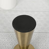 A close-up view of a matte black candle holder with a gold metal base and a small white object in the background.