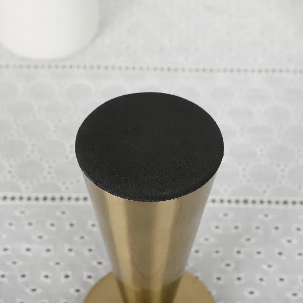 A close-up view of a matte black candle holder with a gold metal base and a small white object in the background.