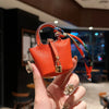 A hand holds an orange mini handbag with a braided wrist strap against a dark background.