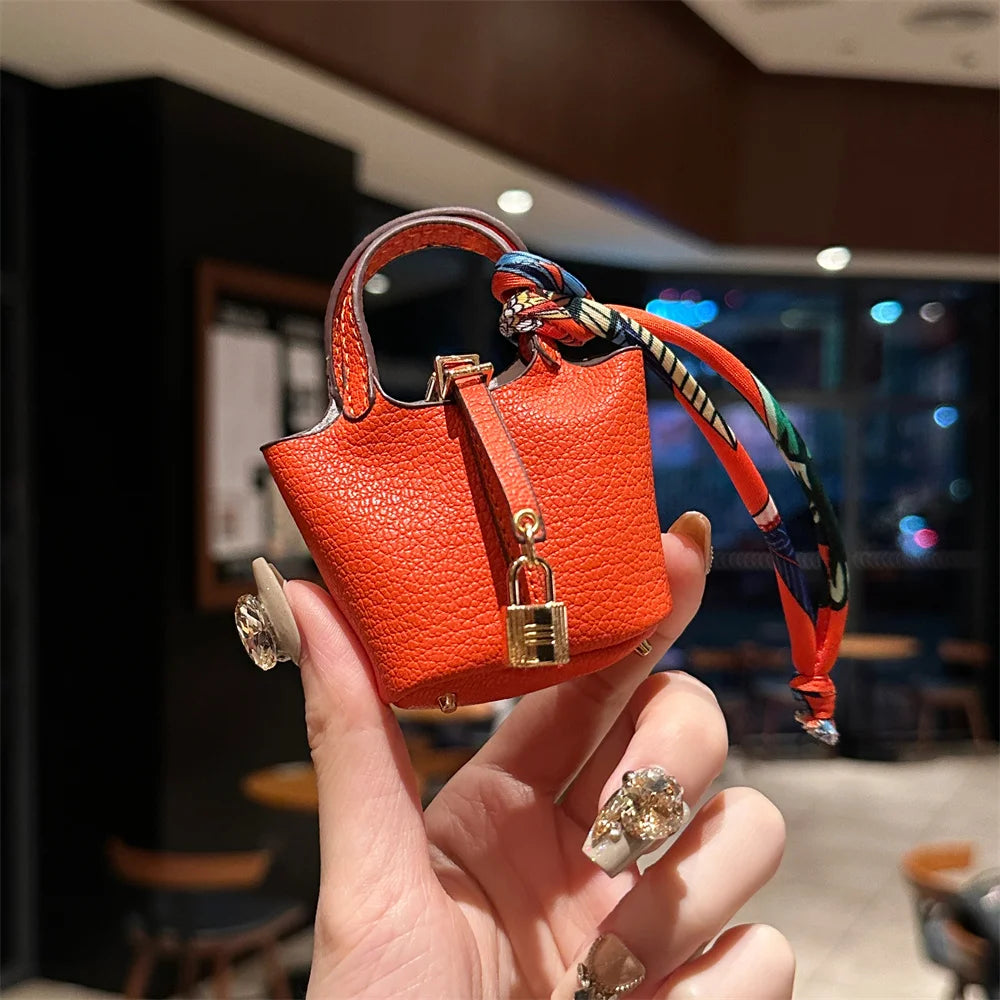 A hand holds an orange mini handbag with a braided wrist strap against a dark background.