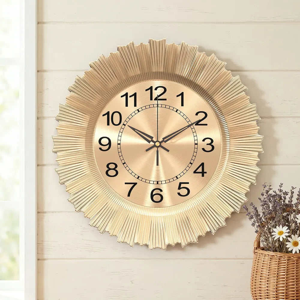 A round gold-toned wall clock with a sunburst design and Roman numerals hanging on a light wooden wall.