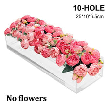 A clear acrylic rectangular vase filled with a dense arrangement of pink roses and greenery.