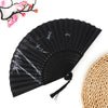 Black vintage bamboo folding fan with silver accents and a pink branch in the background