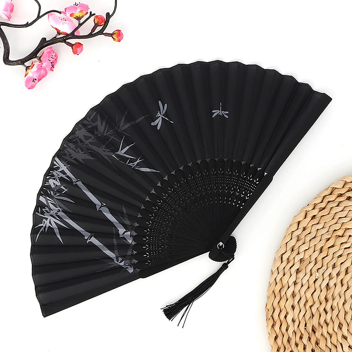 Black vintage bamboo folding fan with silver accents and a pink branch in the background