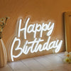 A glowing white LED neon sign spelling out Happy Birthday mounted on a textured wall.