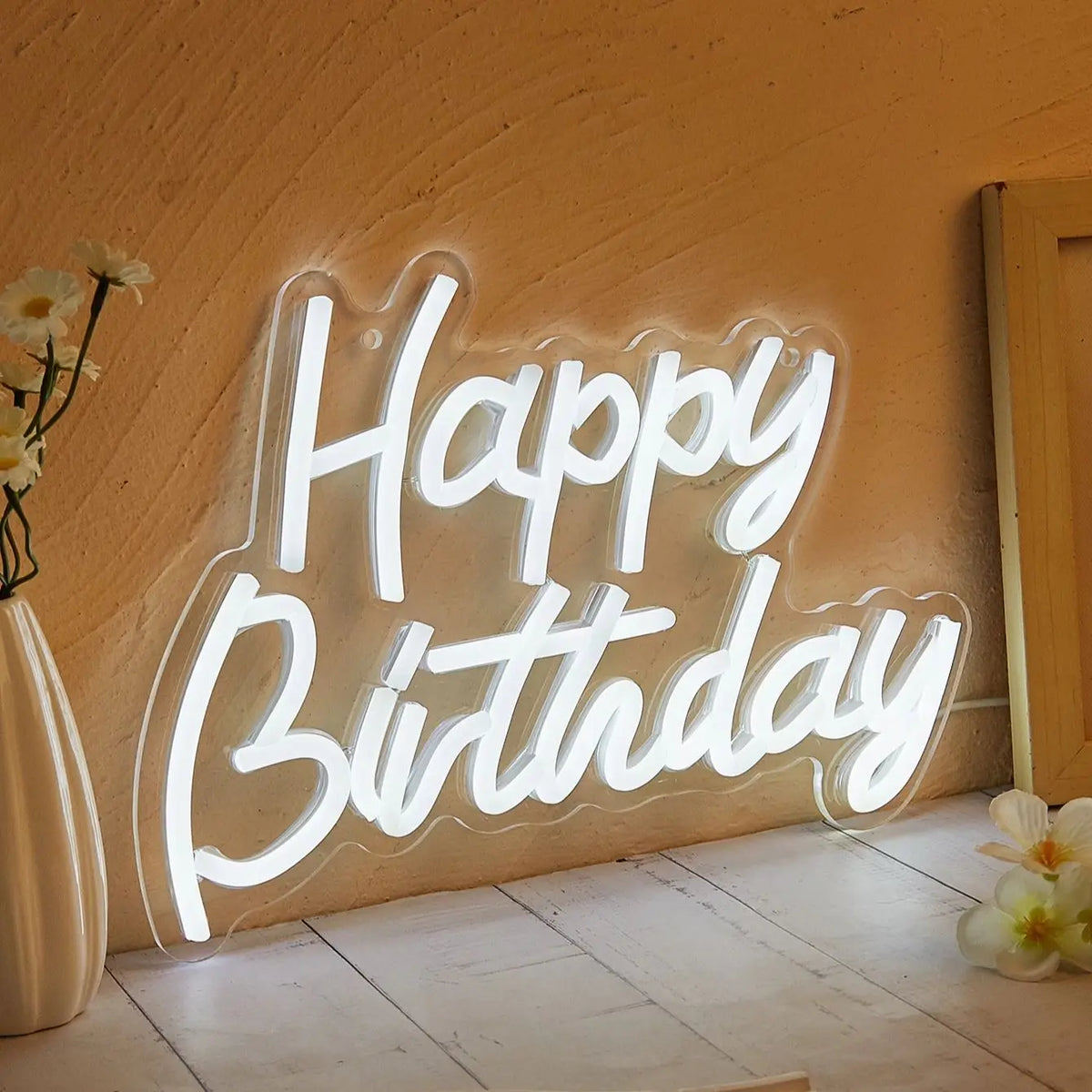 A glowing white LED neon sign spelling out Happy Birthday mounted on a textured wall.