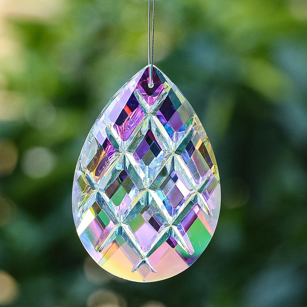 A teardrop-shaped crystal prism with iridescent facets hanging against a blurred green background.