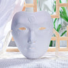 A light gray ancient style masquerade mask with intricate facial details resting on a white textured cloth.