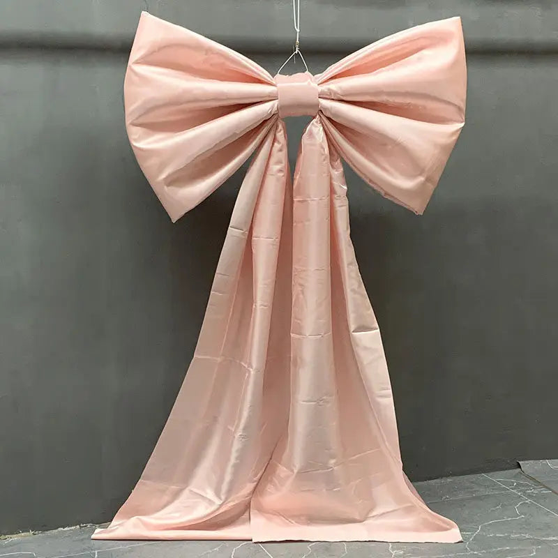 A pink satin bow with a long tulle drape displayed against a gray background for event decor.