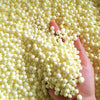 A hand is holding a large quantity of pale yellow foam beads for crafting and decoration.