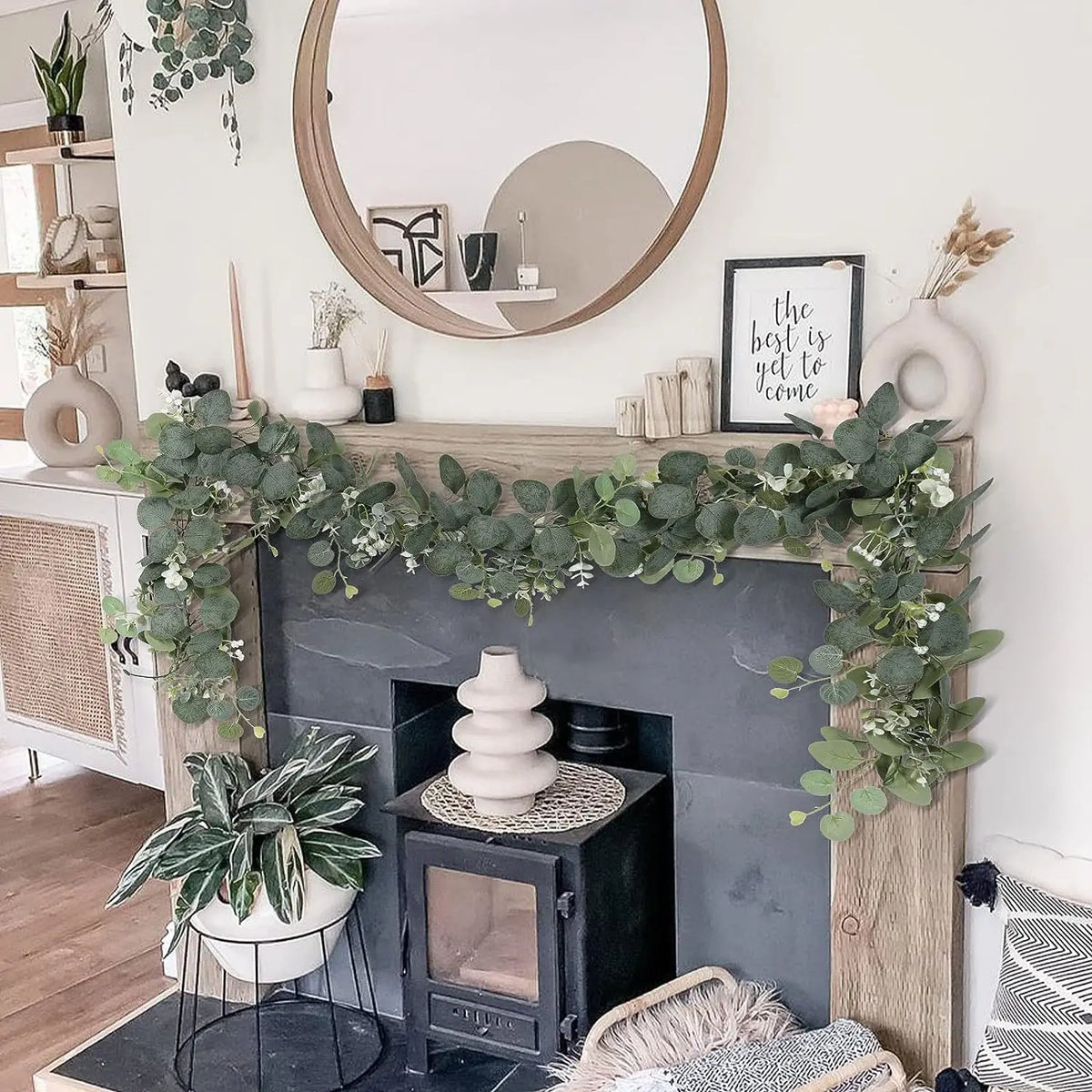 A faux vine garland of green leaves decorates a fireplace mantel with potted plants and rustic accents.