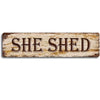 A distressed, rustic metal sign with the text SHE SHED in a serif font.