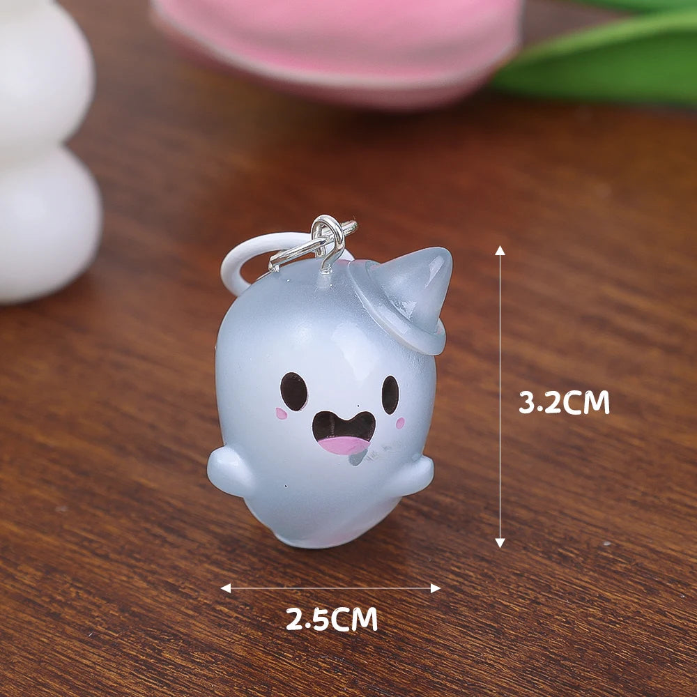 A small, white glow-in-the-dark ghost keychain shaped like a rounded figure resting on a wooden surface.