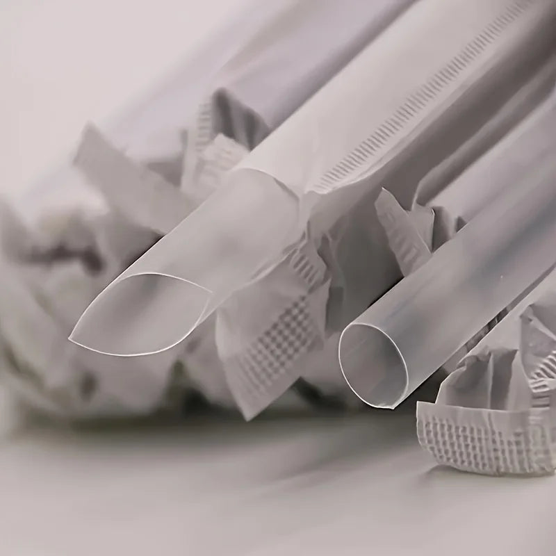 A close-up view of a pack of clear disposable drinking straws lying on a white surface.