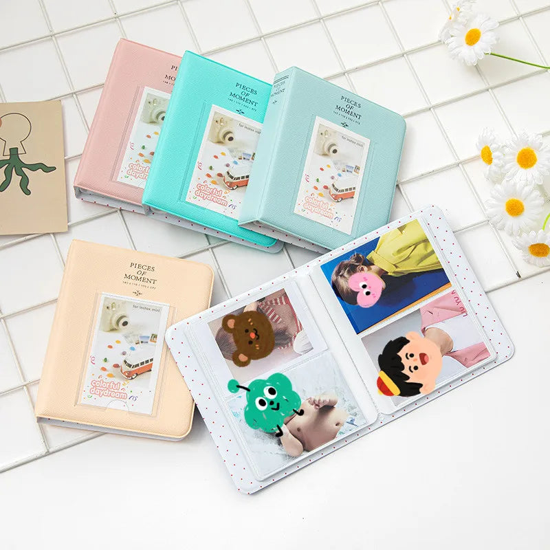A collection of pink, teal, and light green compact photo albums for instant film, displayed on a white tiled surface.