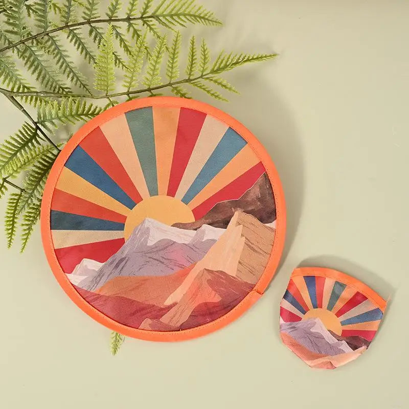 A round fabric art piece featuring a colorful, radiating sun design over mountain landscapes.