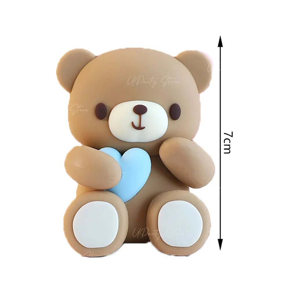 A cute brown teddy bear cake topper with a light blue heart and white accents.