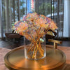 A bouquet of iridescent gold foil artificial roses displayed in a clear glass vase on a round gold tray.