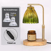 A brass adjustable candle warmer lamp with a glass shade and heating bulbs, shown next to a timer and a wooden base.